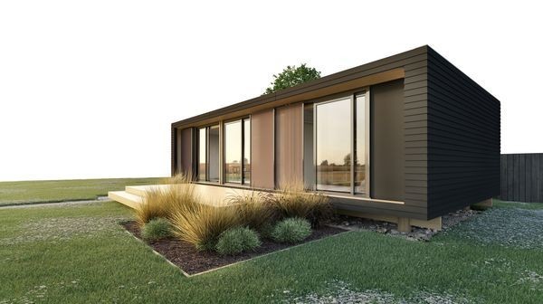 Modern flat-roofed house with large glass windows, surrounded by green grass and ornamental shrubs.